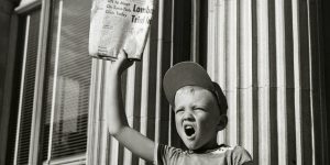 Boy selling newspapers in front of a building